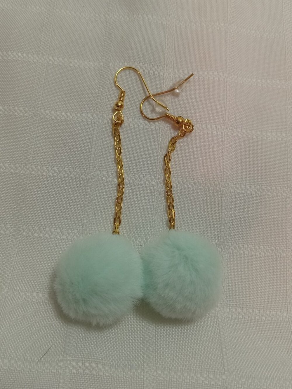 Handmade earrings with small pom-poms and gold-colored accent hooks and chains